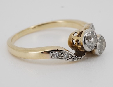 A diamond toi-et-moi ring, early 20th century, collet-set with two circular-cut diamonds totalling approximately 0.30 carats, to sinuous shoulders set with single-cut diamonds, size K, stamped 18ct PLAT, Condition: good